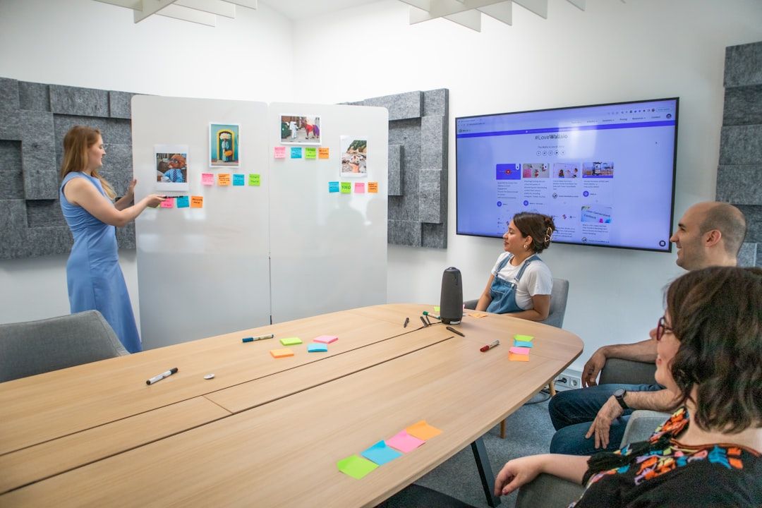 Чотири колеги обговорюють ідеї біля дошки з фото та стікерами, великий екран показує вебсторінку.